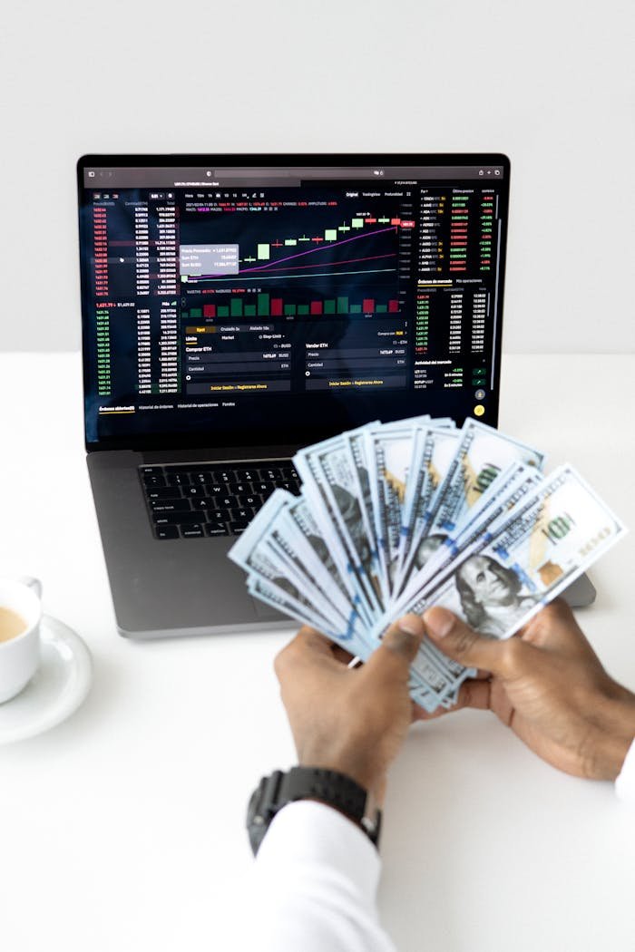 services-bg Hands holding cash in front of a laptop displaying stock market data, symbolizing financial growth and investment.